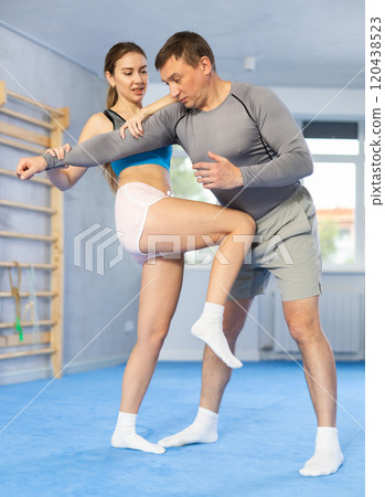 Young woman learns to fight back against an attacking man during self-defense training at gym Young woman learns to fight back against an attacking man during self-defense training at gym 120438523