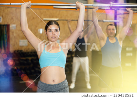 Concentrated young woman performing exercises with barbell 120438581