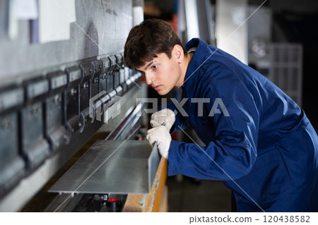 Young worker operating metal press brake in industrial workshop Young worker operating metal press brake in industrial workshop 120438582