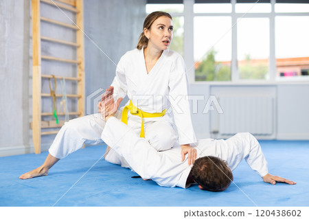 Young woman wearing kimono applying arm twist technique against middle-aged man Young woman wearing kimono applying arm twist technique against middle-aged man 120438602