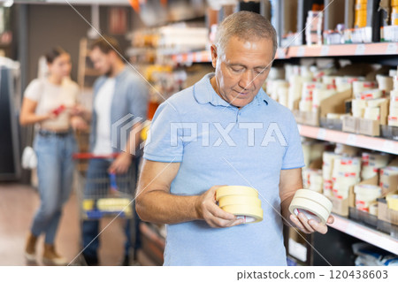 Elderly man chooses building tape in store 120438603