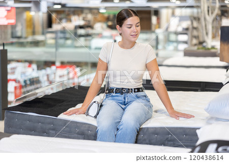 In furniture store, girl examines orthopedic mattress. In furniture store, girl examines orthopedic mattress. 120438614