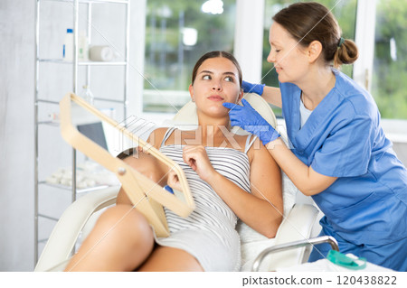 Woman cosmetologist examines patients nasolabial area after lifting procedure and palpates lips mouth Woman cosmetologist examines patients nasolabial area after lifting procedure and palpates lips mouth 120438822