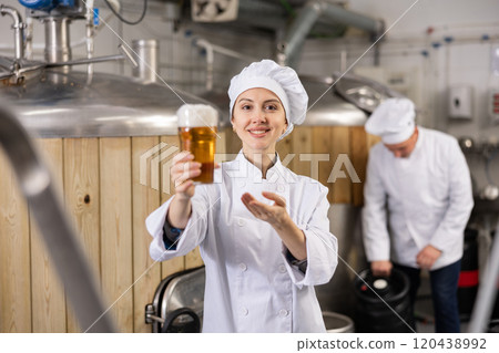 Portrait of female brewer who is standing with glass of beer on his workplace in brew-house 120438992