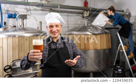Successful brewmaster holding glass of foamy pale ale Successful brewmaster holding glass of foamy pale ale 120439035