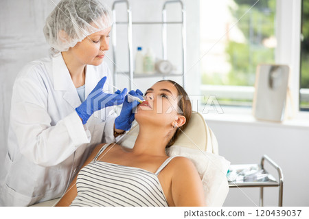 Adult woman cosmetologist makes injection in lips of patient Adult woman cosmetologist makes injection in lips of patient 120439037