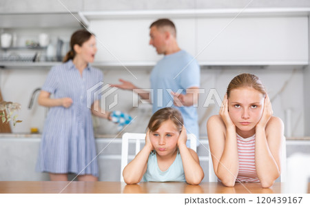 Upset teenage girls sitting in kitchen while parents quarreling Upset teenage girls sitting in kitchen while parents quarreling 120439167