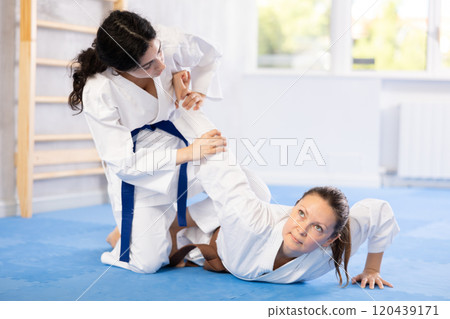Sportive woman holds her opponent by force while sitting on mats during judo classes 120439171