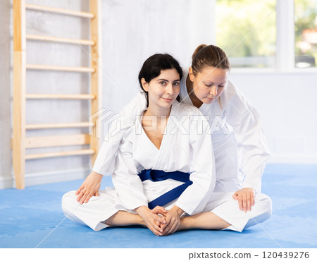 Woman stretching in butterfly pose with help of trainer Woman stretching in butterfly pose with help of trainer 120439276