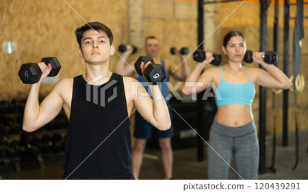 Focused guy performing arm and shoulder workout with dumbbells 120439291