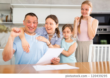 Cheerful man with wife and teenage daughters reading some papers Cheerful man with wife and teenage daughters reading some papers 120439295