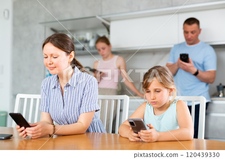 Mom sitting near kitchen table next to younger daughter with phones playing online game Mom sitting near kitchen table next to younger daughter with phones playing online game 120439330