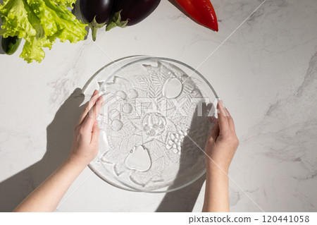 A person holds a glass plate with vegetables behind them 120441058