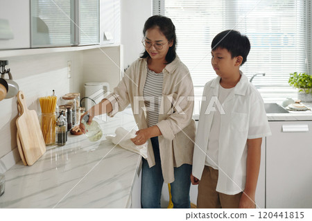 Cleaning Kitchen Counter with Child Standing Nearby 120441815