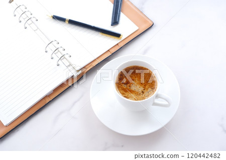 一張圖片：某人在辦公桌前使用筆記本工作，同時喝著加大量牛奶的咖啡或拿鐵咖啡。 120442482