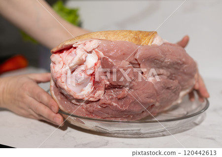 A large, raw pork shoulder is placed on a glass plate and is ready for cooking now 120442613