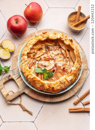 Homemade apple tart with almond toppings on a wooden board surrounded by fresh apples and cinnamon Homemade apple tart with almond toppings on a wooden board surrounded by fresh apples and cinnamon 120443152
