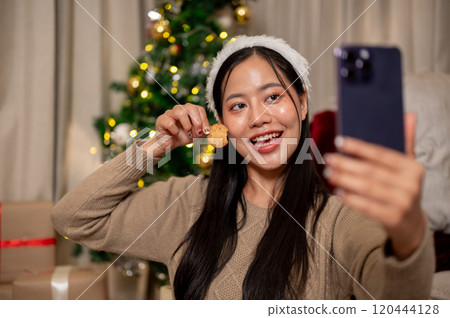 A cheerful Asian woman takes a selfie while happily celebrating the Christmas holiday alone at home. 120444128