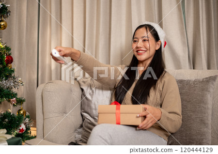 A cheerful woman celebrates the Christmas holiday alone at home, enjoying watching TV on the sofa. 120444129