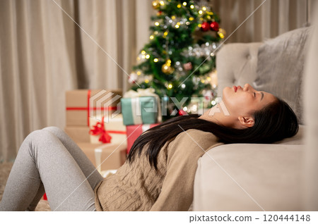 A carefree, calm Asian woman in cozy warm clothes takes a peaceful nap in the living room. A carefree, calm Asian woman in cozy warm clothes takes a peaceful nap in the living room. 120444148
