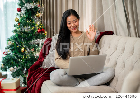 A cheerful Asian woman enjoys talking on a video call through her laptop on the Christmas holiday. A cheerful Asian woman enjoys talking on a video call through her laptop on the Christmas holiday. 120444596