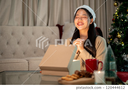 A beautiful woman makes a Christmas wish with her eyes closed, celebrating Christmas night at home. 120444612