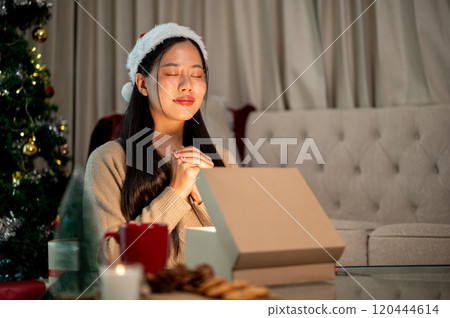 A beautiful woman makes a Christmas wish with her eyes closed, celebrating Christmas night at home. 120444614