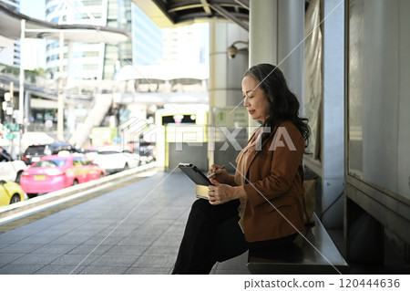 Mature businessman using digital tablet sitting at a modern urban station Mature businessman using digital tablet sitting at a modern urban station 120444636