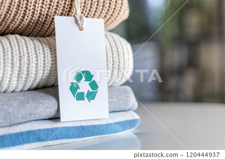 Knitted warm clothes neatly folded heap with craft tag recycling material circle arrow closeup 120444937