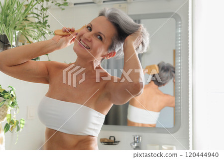 Portrait funny mature gray haired woman at light bathroom with hairbrush closeup Portrait funny mature gray haired woman at light bathroom with hairbrush closeup 120444940