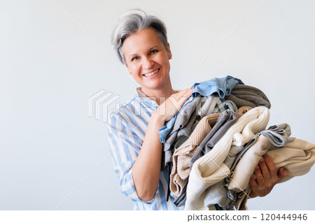 Mature gray haired woman holding stack of clothes isolated on white background 120444946
