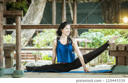 Girl sitting doing split meditation yoga outdoors, woman doing side split yoga outdoors, young woman doing side split yoga 120445339