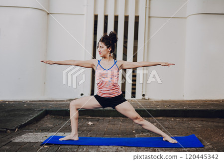 Girl practicing yoga Warrior II pose outdoors. Latin woman doing yoga warrior pose outdoors. Young woman doing yoga virabhadrasana II outdoors 120445342