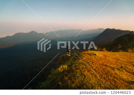 A man hiking stands on a mountain cliff. 120446023