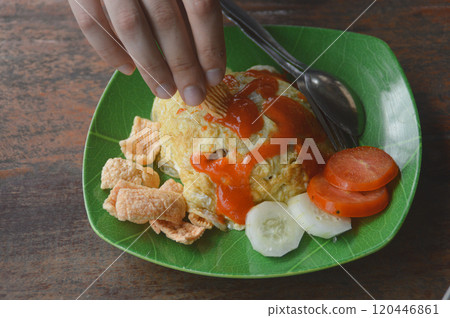Hand dipping kropek or cracker in ketchup as part of nasi goreng or fried rice topped with omelette called dadar telur padang, authentic local food of Indonesia Hand dipping kropek or cracker in ketchup as part of nasi goreng or fried rice topped with omelette called dadar telur padang, authentic local food of Indonesia 120446861