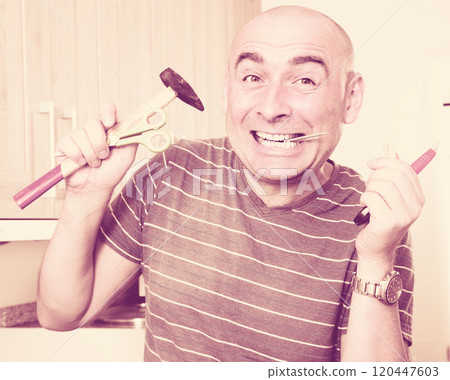 imposing man in prime of life holds in teeth of screws and holding hammer imposing man in prime of life holds in teeth of screws and holding hammer 120447603