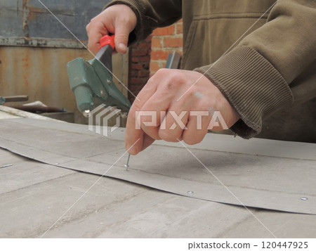 inserting a thin long aluminum rivet into a metal structure, the worker's hands holding the fastener and riveter inserting a thin long aluminum rivet into a metal structure, the worker's hands holding the fastener and riveter 120447925