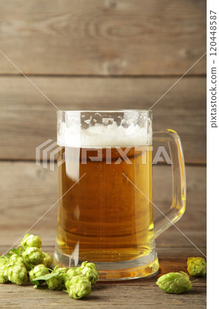 Glass of fresh beer with green hops on a grey background. Vertical photo 120448587