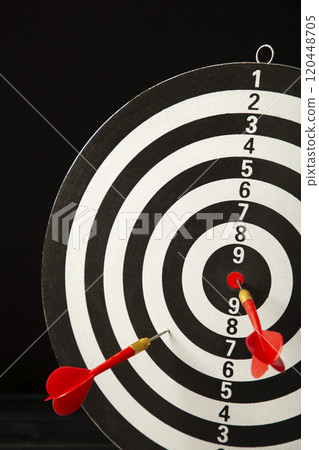 Dart board with red darts on black background. Vertical photo. Dart board with red darts on black background. Vertical photo. 120448705