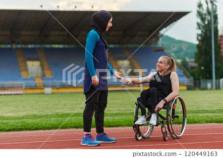 A Muslim woman wearing a burqa supports her friend with disability in a wheelchair as they train together on a marathon course. A Muslim woman wearing a burqa supports her friend with disability in a wheelchair as they train together on a marathon course. 120449163