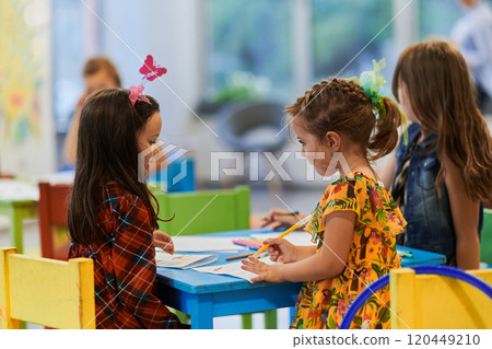 Creative kids during an art class in a daycare center or elementary school classroom drawing with female teacher. 120449210