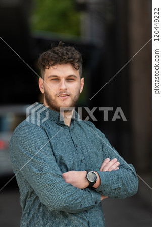 A successful young businessman in a shirt, with crossed arms, poses outdoors, confident expression on his face. A successful young businessman in a shirt, with crossed arms, poses outdoors, confident expression on his face. 120449222