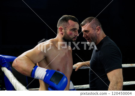 Cornered boxer receives strategic advice from trainer during intense bout. Cornered boxer receives strategic advice from trainer during intense bout. 120450004