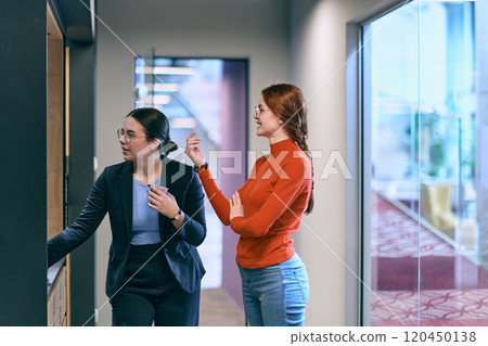 Amidst the contemporary and spacious office setting, two modern young women engage in conversation during a work break, reflecting the importance of relaxation and collaboration in the dynamic 120450138