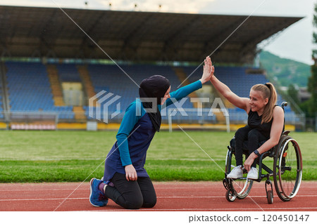 A Muslim woman wearing a burqa supports her friend with disability in a wheelchair as they train together on a marathon course. 120450147