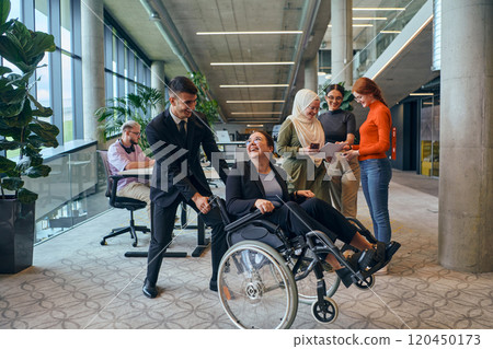 A diverse group of business colleagues is having fun with their wheelchair-using colleague, demonstrating their attention and inclusivity in the workplace 120450173
