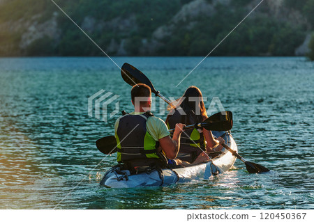 A young couple enjoying an idyllic kayak ride in the middle of a beautiful river surrounded by forest greenery in sunset time A young couple enjoying an idyllic kayak ride in the middle of a beautiful river surrounded by forest greenery in sunset time 120450367