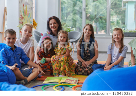 A happy female teacher sitting and playing hand games with a group of little schoolchildren 120450382