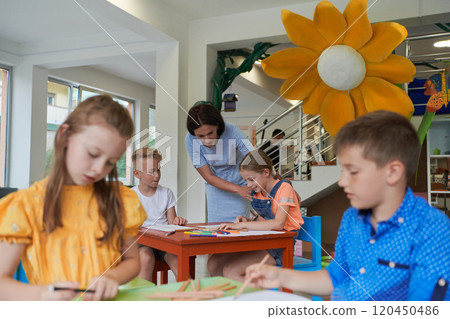 Creative kids during an art class in a daycare center or elementary school classroom drawing with female teacher. 120450486