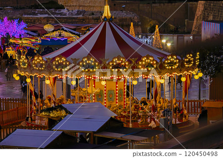 Brightly lit vintage carousel with a red and white striped canopy surrounded by glowing lights and festive decorations at night Brightly lit vintage carousel with a red and white striped canopy surrounded by glowing lights and festive decorations at night 120450498